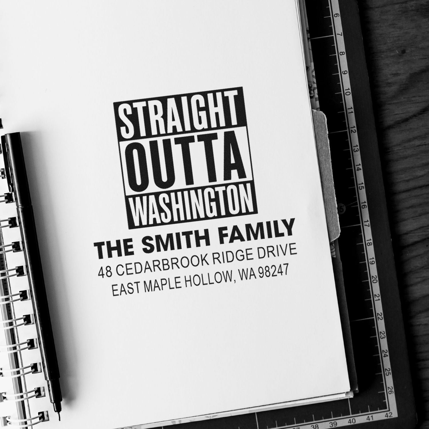 Custom address stamp reading Straight Outta Washington on a notebook page, beside a pen and ruler on a desk.