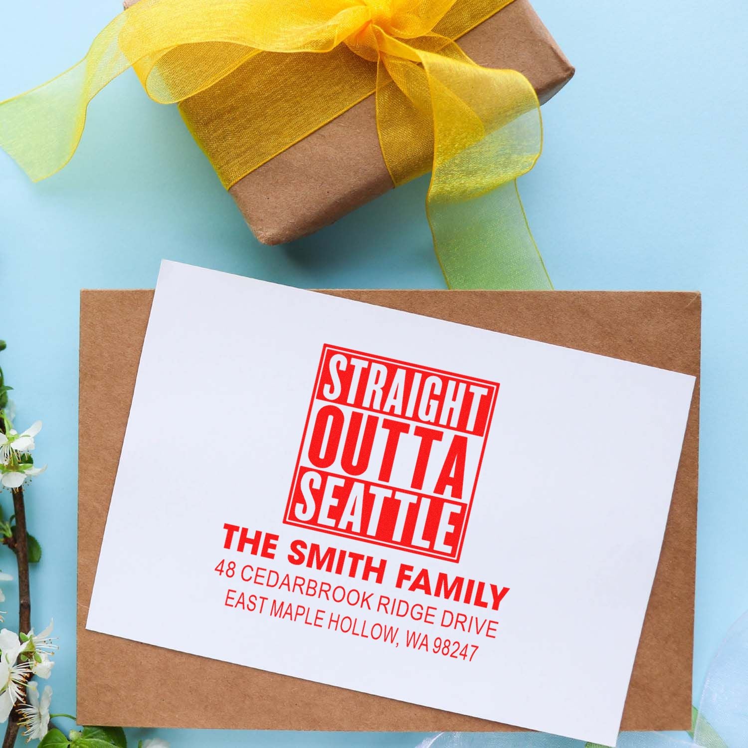 Custom self-inking address stamp with Straight Outta Seattle design on a white card atop a kraft envelope, beside a ribbon-wrapped gift.