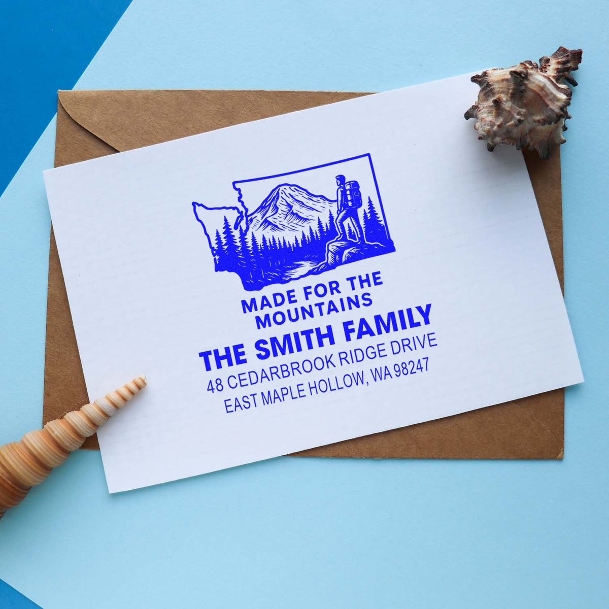 Custom return address stamp for The Smith Family, blue mountain hiking design on a white card with envelope and seashell accents.