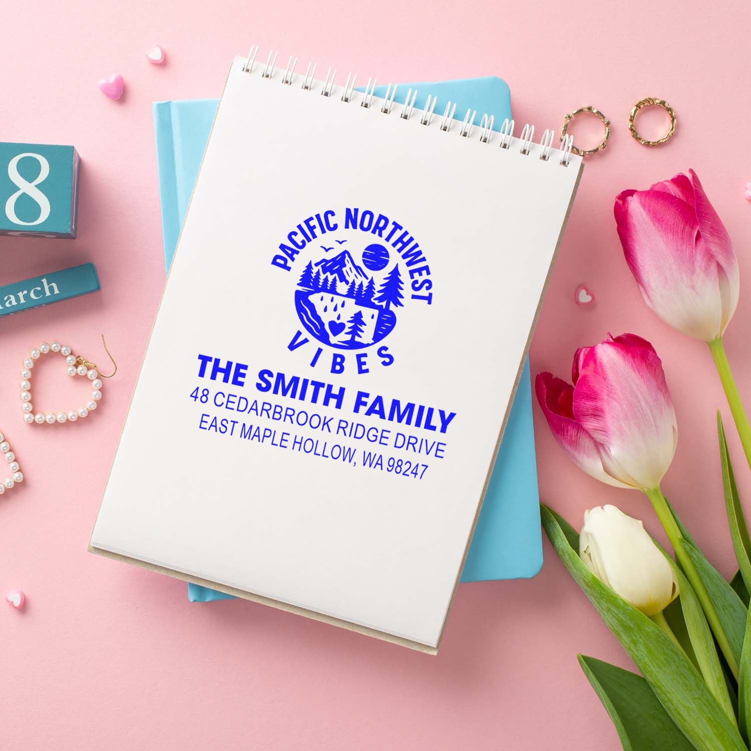Personalized return address stamp for The Smith Family on spiral notebook, styled with tulips, rings and pastel pink decor.
