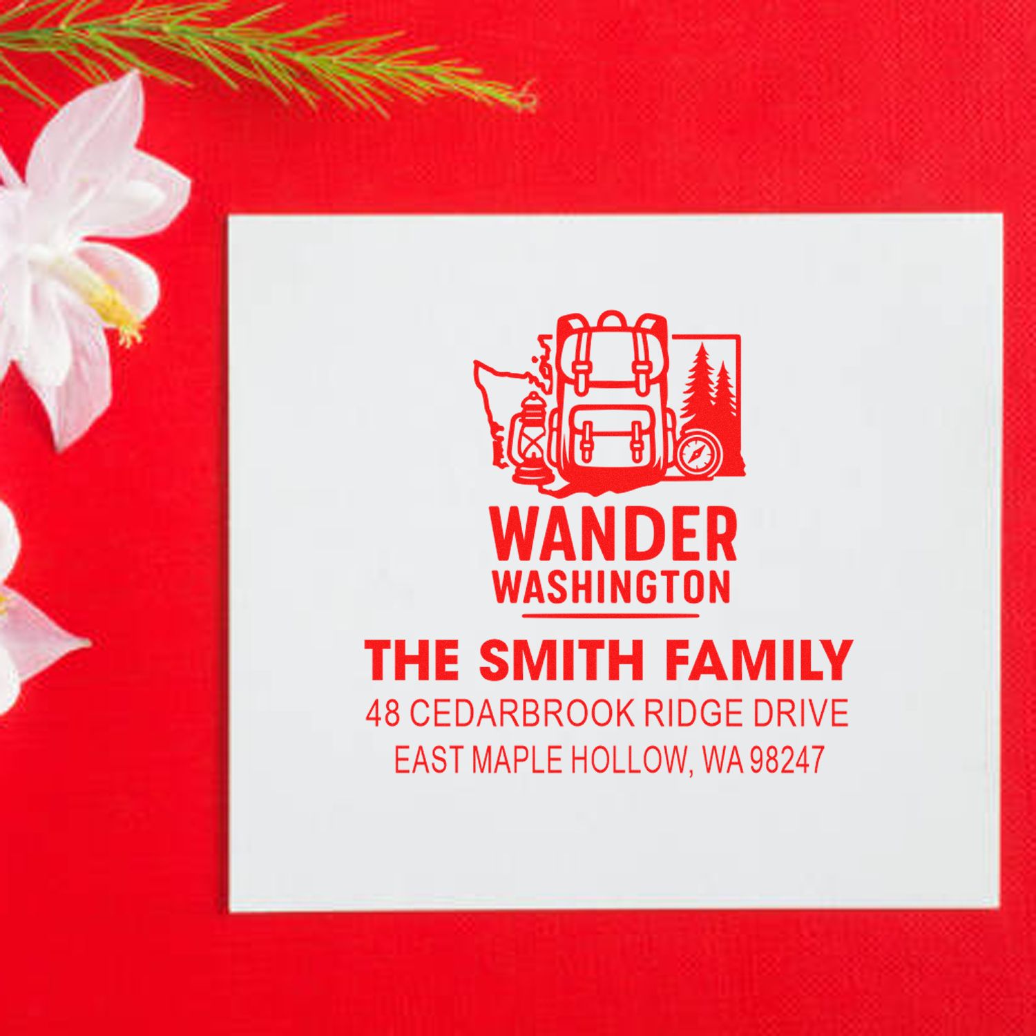 Custom family address stamp for Washington with backpack and compass design, displayed on white card against a red holiday backdrop.