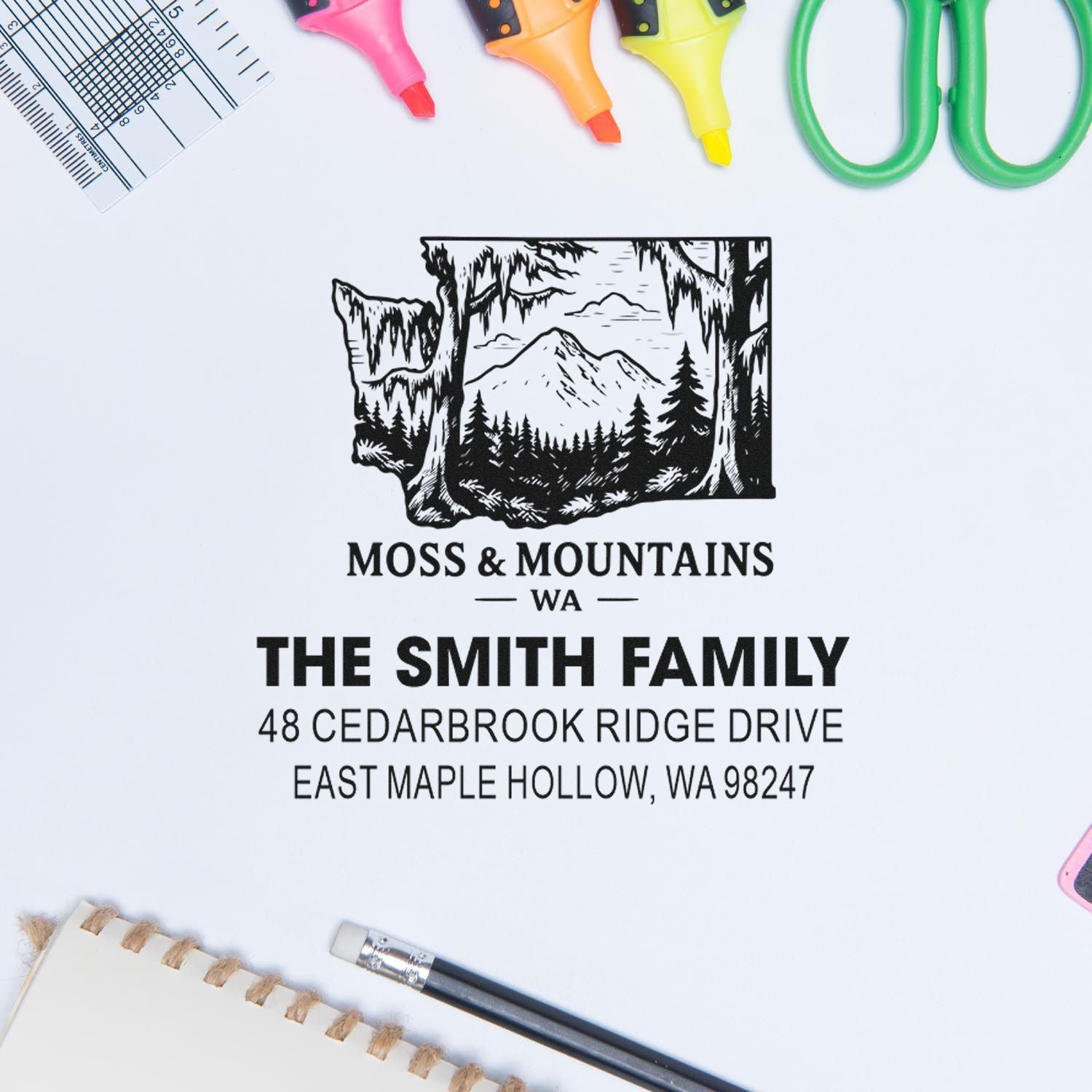 Custom self-inking address stamp with mountain forest logo for The Smith Family on a white desk, surrounded by stationery tools.