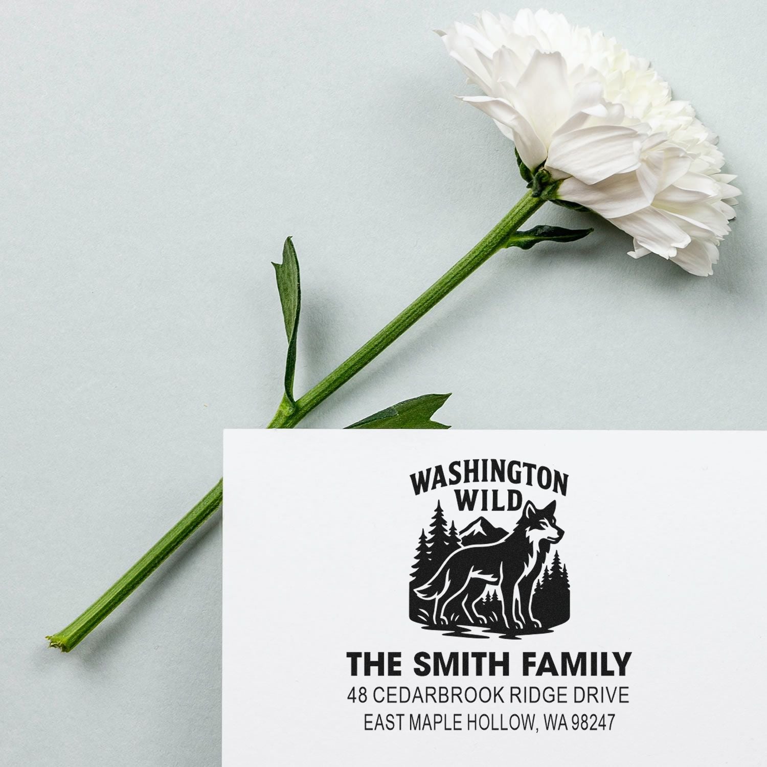Personalized Washington Wild return address stamp with wolf and pine design beside a white flower on a light gray background.