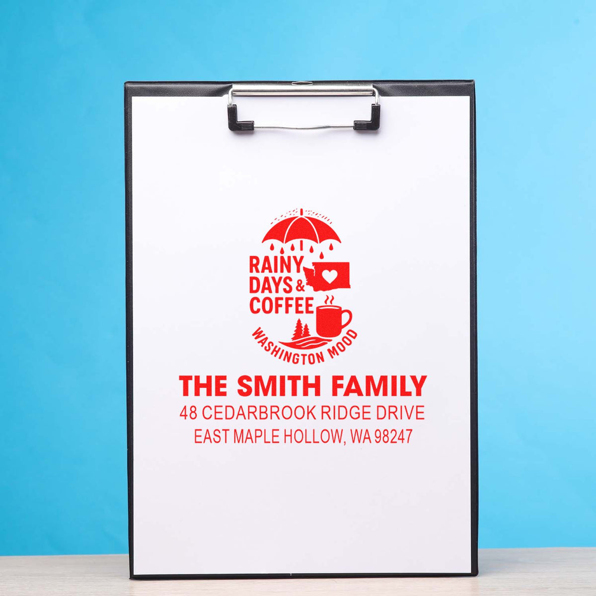 Custom address stamp on clipboard with red Rainy Days & Coffee Washington Mood design and The Smith Family address on blue background.