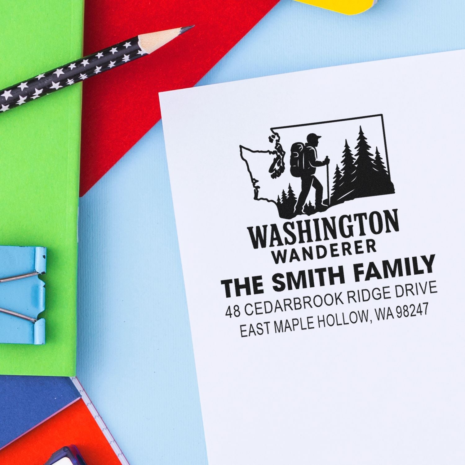 Personalized Washington Wanderer return address stamp with hiker silhouette on white card, surrounded by colorful stationery and a star-pattern pencil.