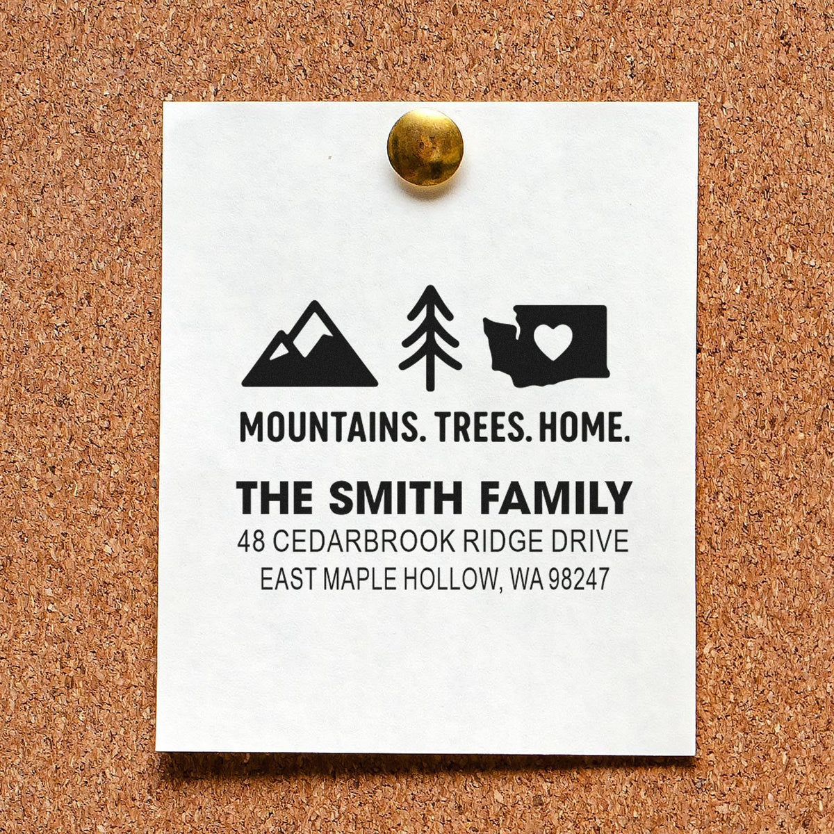 Custom address stamp on a white card pinned to a corkboard, featuring mountains, trees, home icons, and The Smith Family address.