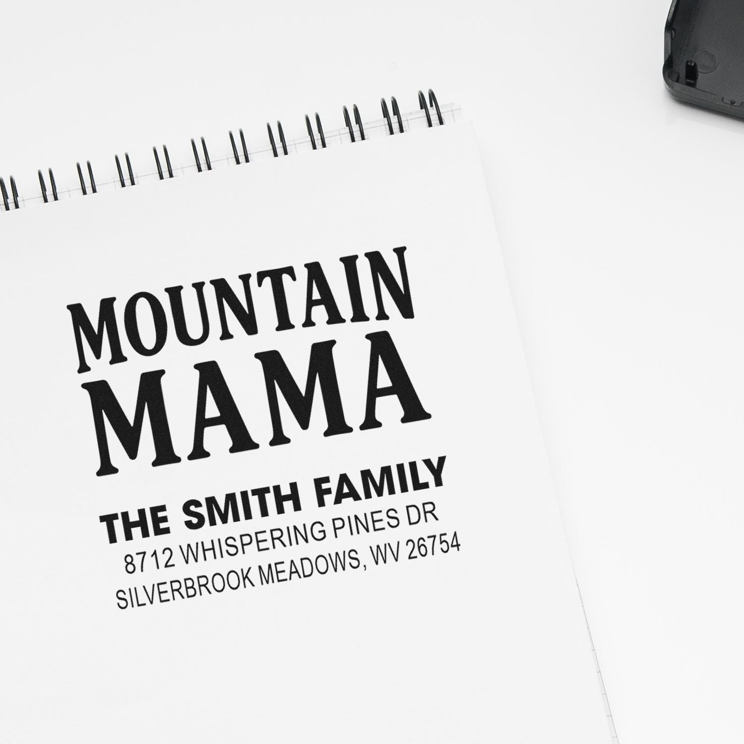 Custom return address stamp reading Mountain Mama for The Smith Family on a white spiral notepad with black ink.