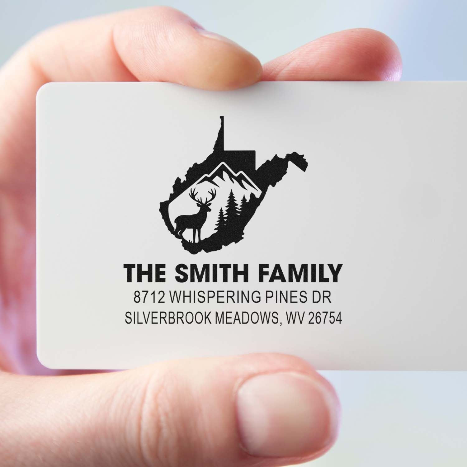 Hand holding custom family address stamp with West Virginia silhouette, deer and mountains, featuring The Smith Family address.