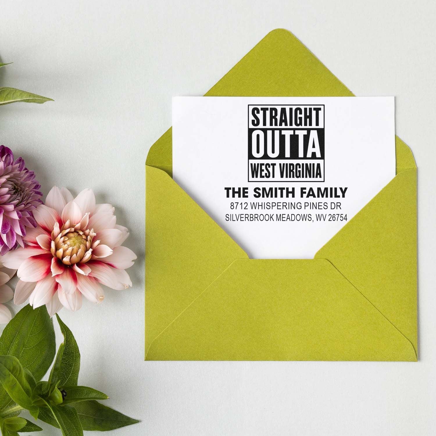 Custom address stamp reading Straight Outta West Virginia for The Smith Family, displayed in a lime green envelope with flowers on a white tabletop.