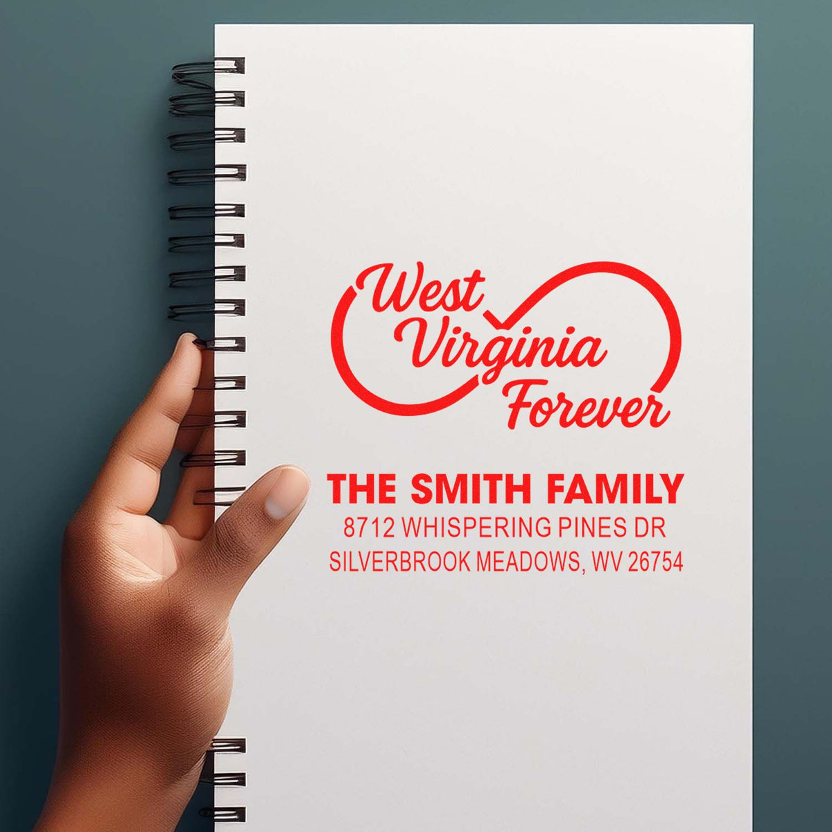 Custom West Virginia Forever address stamp on a spiral-bound notebook, held by hand, featuring The Smith Family and WV address in red.
