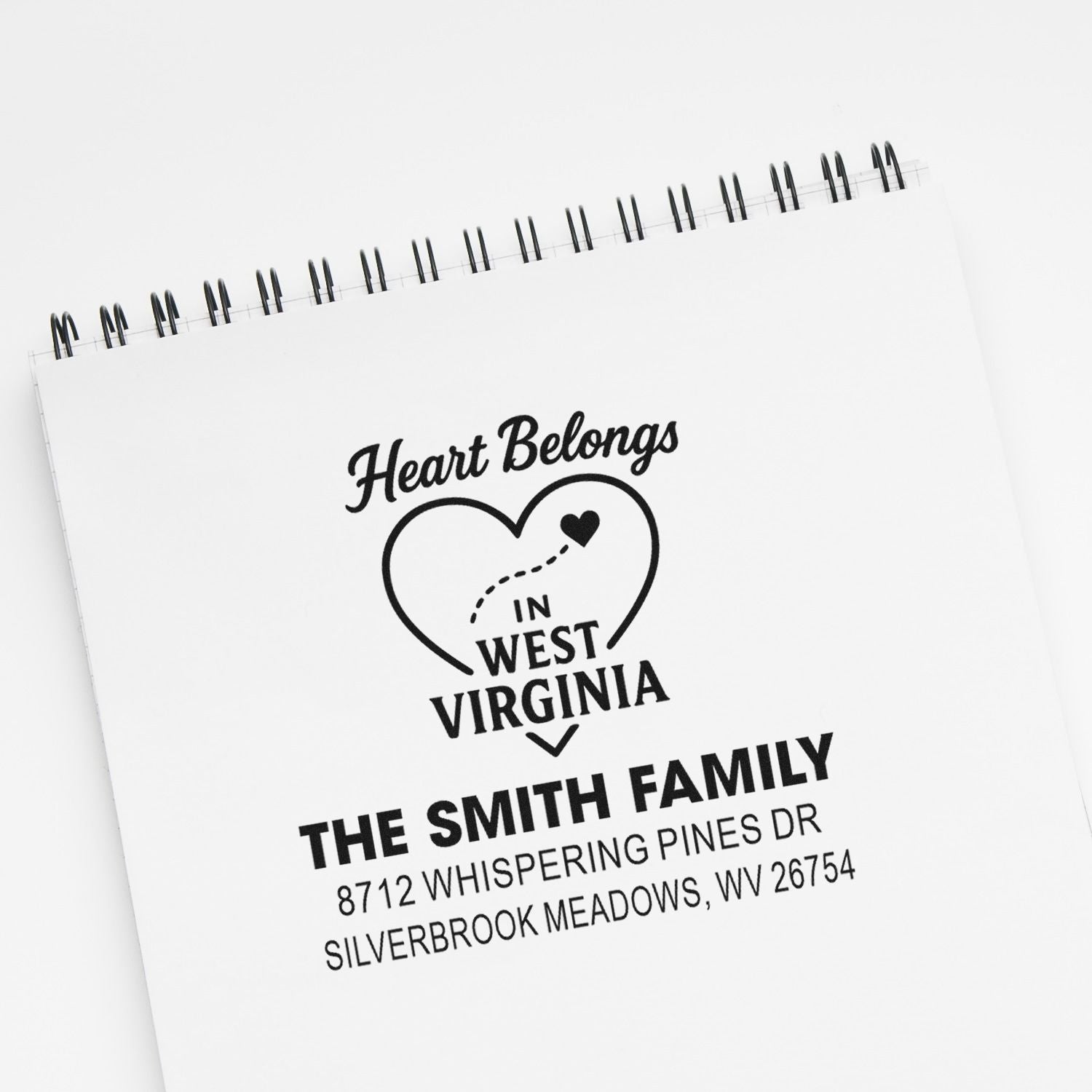 Custom family address stamp with heart graphic and Heart Belongs in West Virginia, shown on a spiral notebook mockup.
