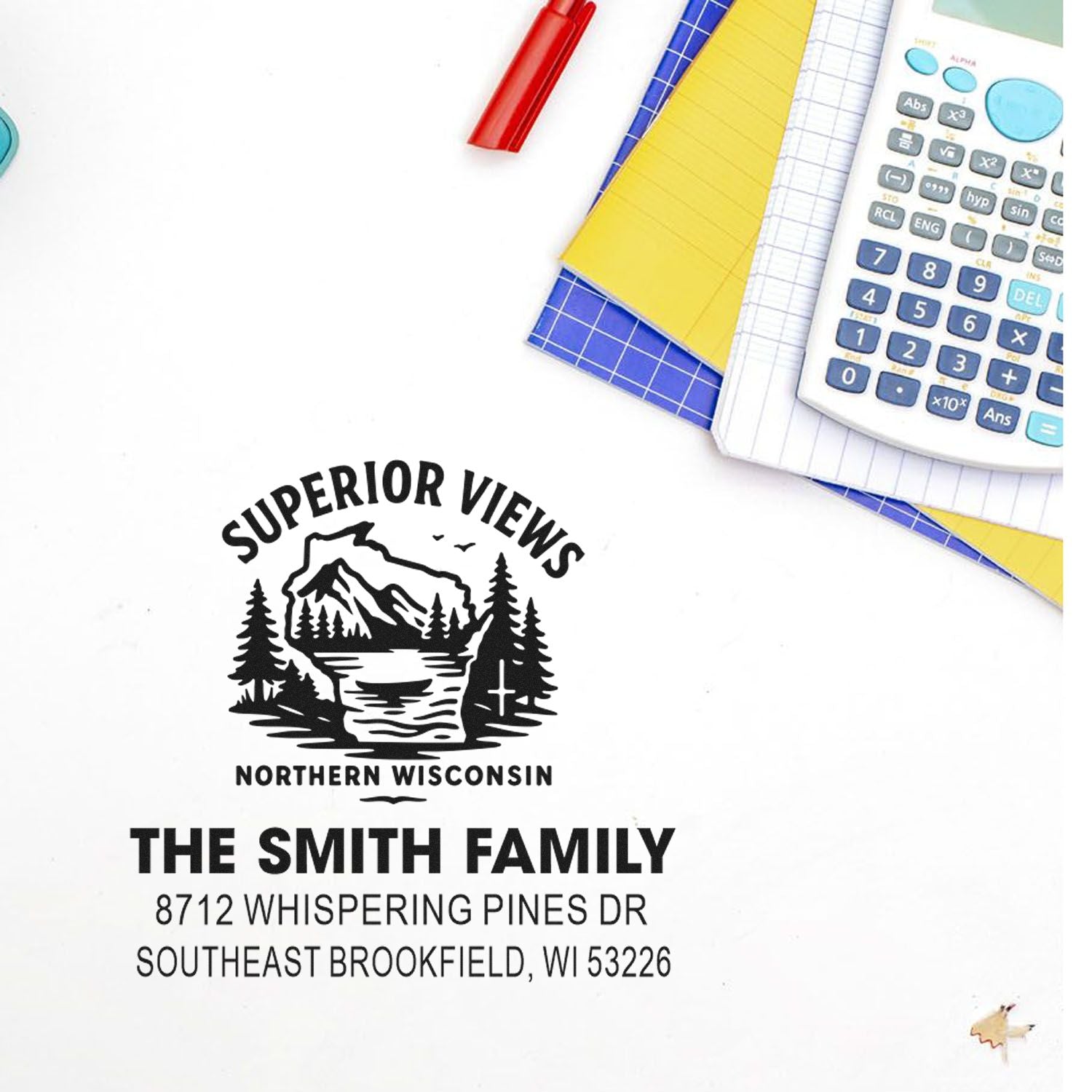 Custom address stamp for The Smith Family with Northern Wisconsin mountain logo, printed on white paper beside calculator, notebooks, and pen.