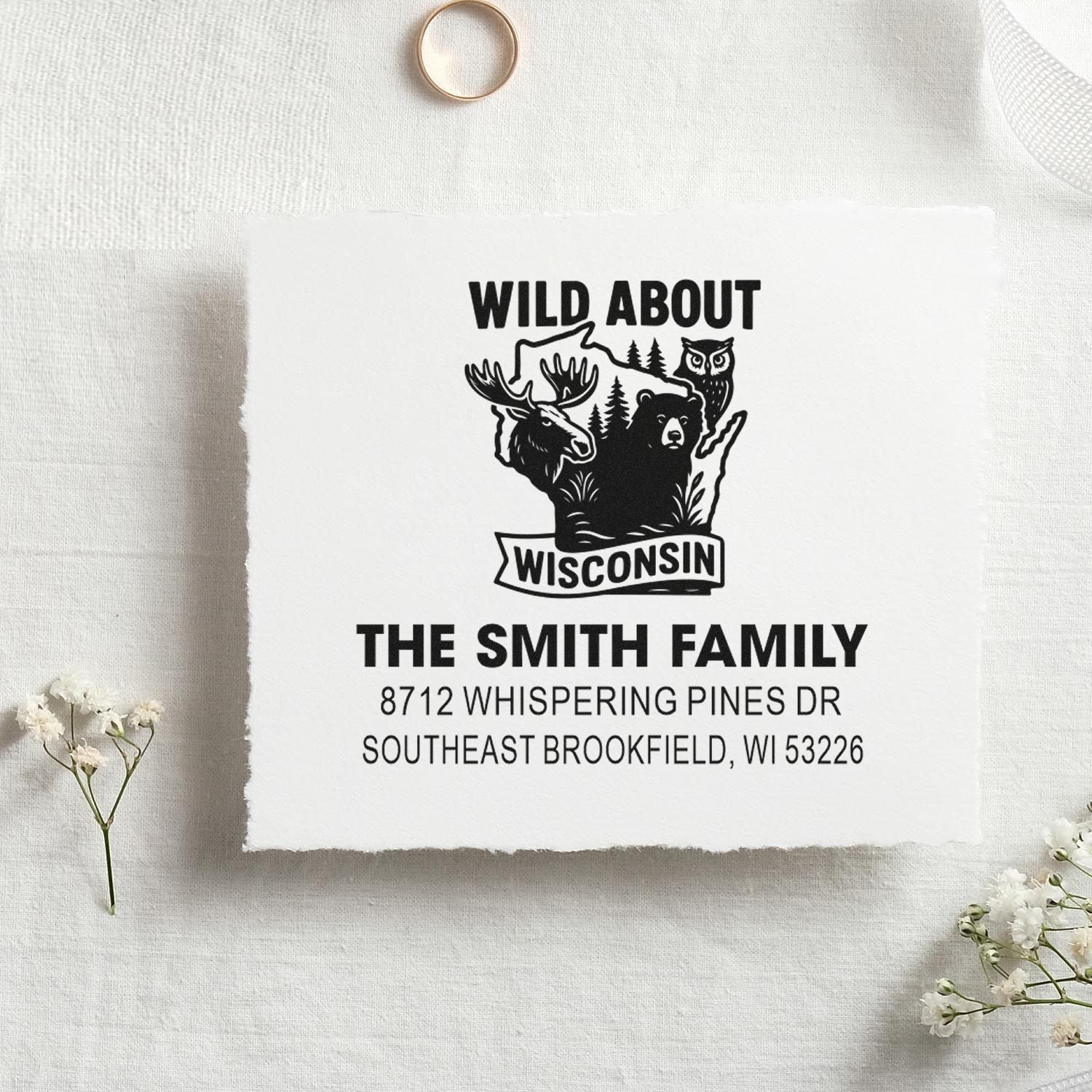Custom Wisconsin family address stamp on white paper swatch, featuring moose, bear and owl with Wild About Wisconsin design in rustic flat lay.
