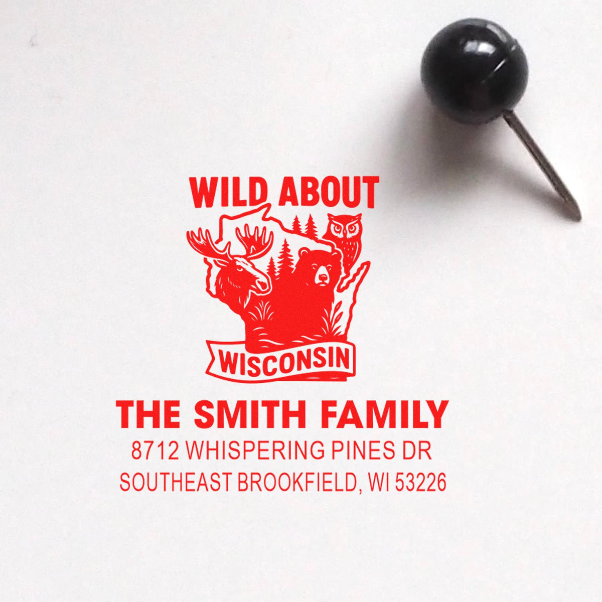 Custom rubber stamp on white paper reading Wild About Wisconsin with moose, bear and owl, plus The Smith Family address; black stamp tool nearby.