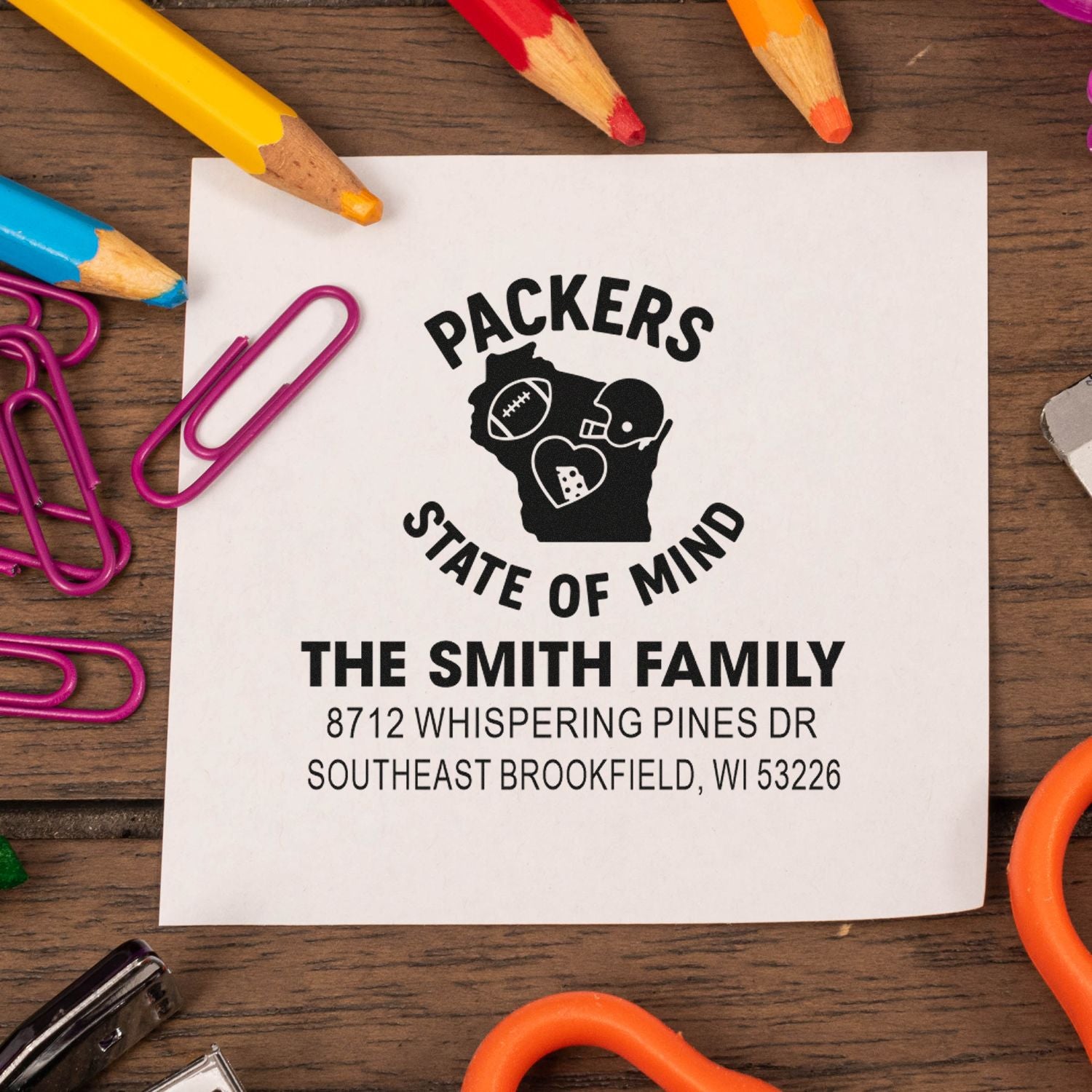 Custom Packers State of Mind address stamp on white paper, surrounded by colorful pencils and paper clips on a wooden desk.