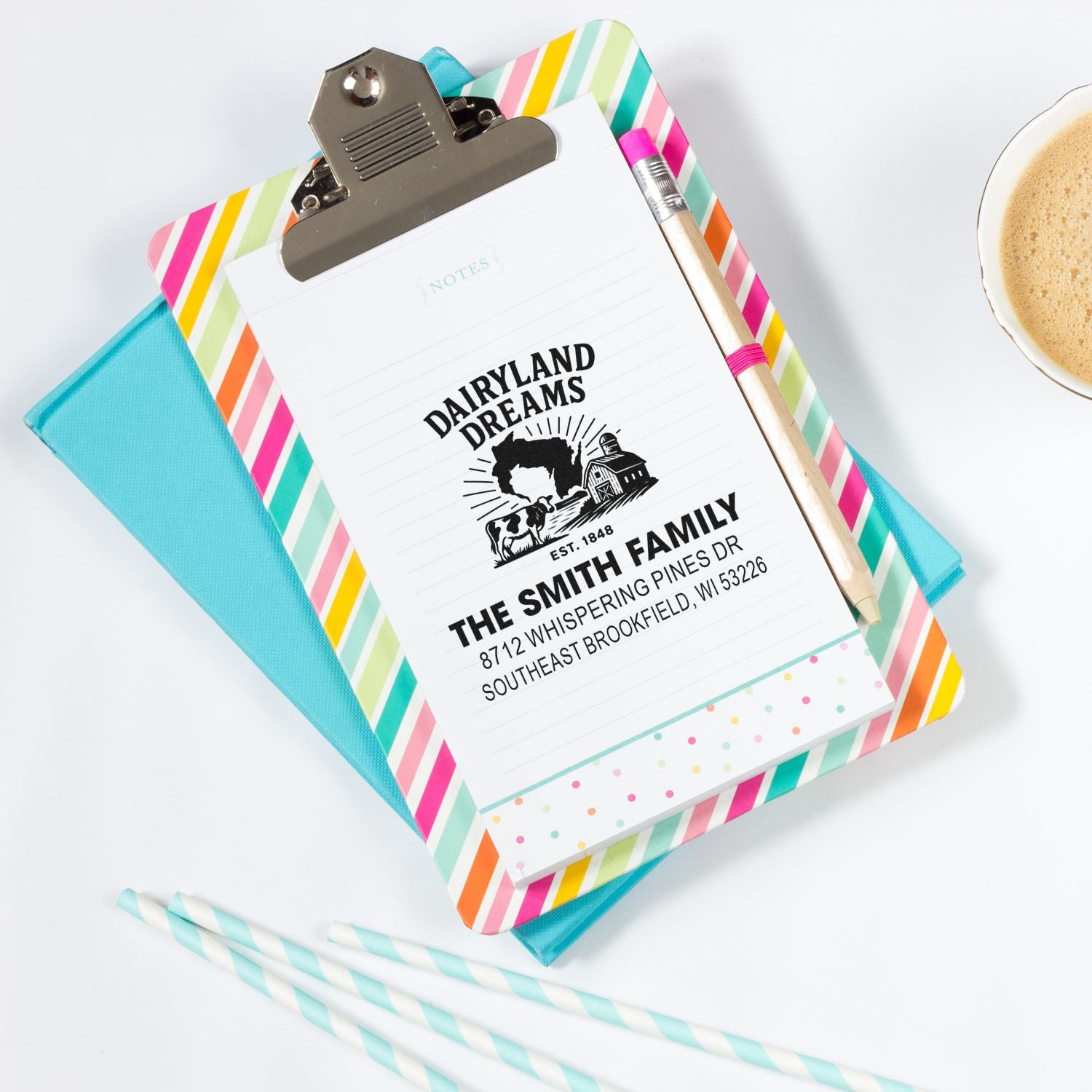 Custom family address stamp on a colorful clipboard, with pencil, notebook, and coffee on a white desk.