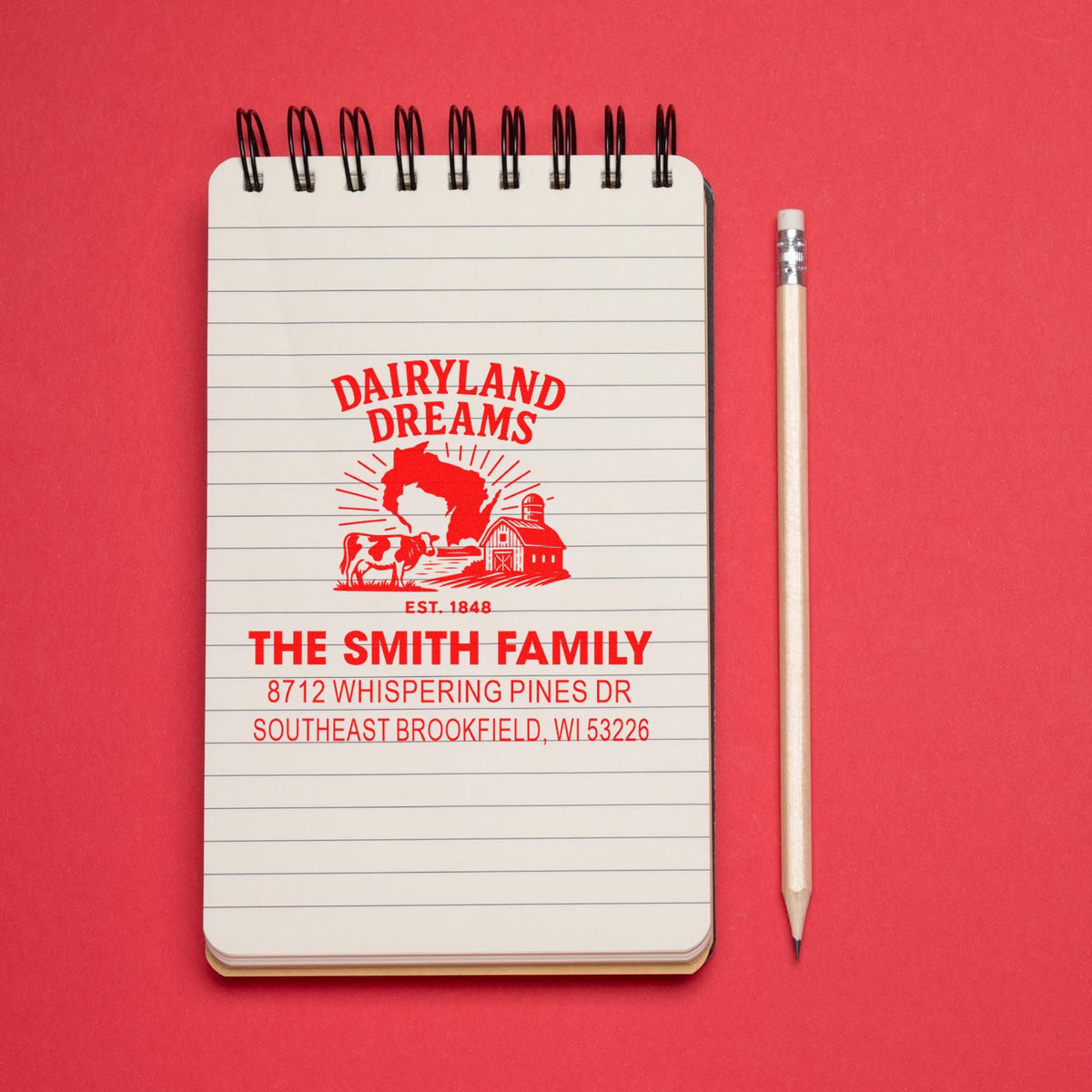 Custom farm-themed address stamp on spiral notepad with pencil, featuring Dairyland Dreams, The Smith Family, and barn-and-cow artwork on red background.