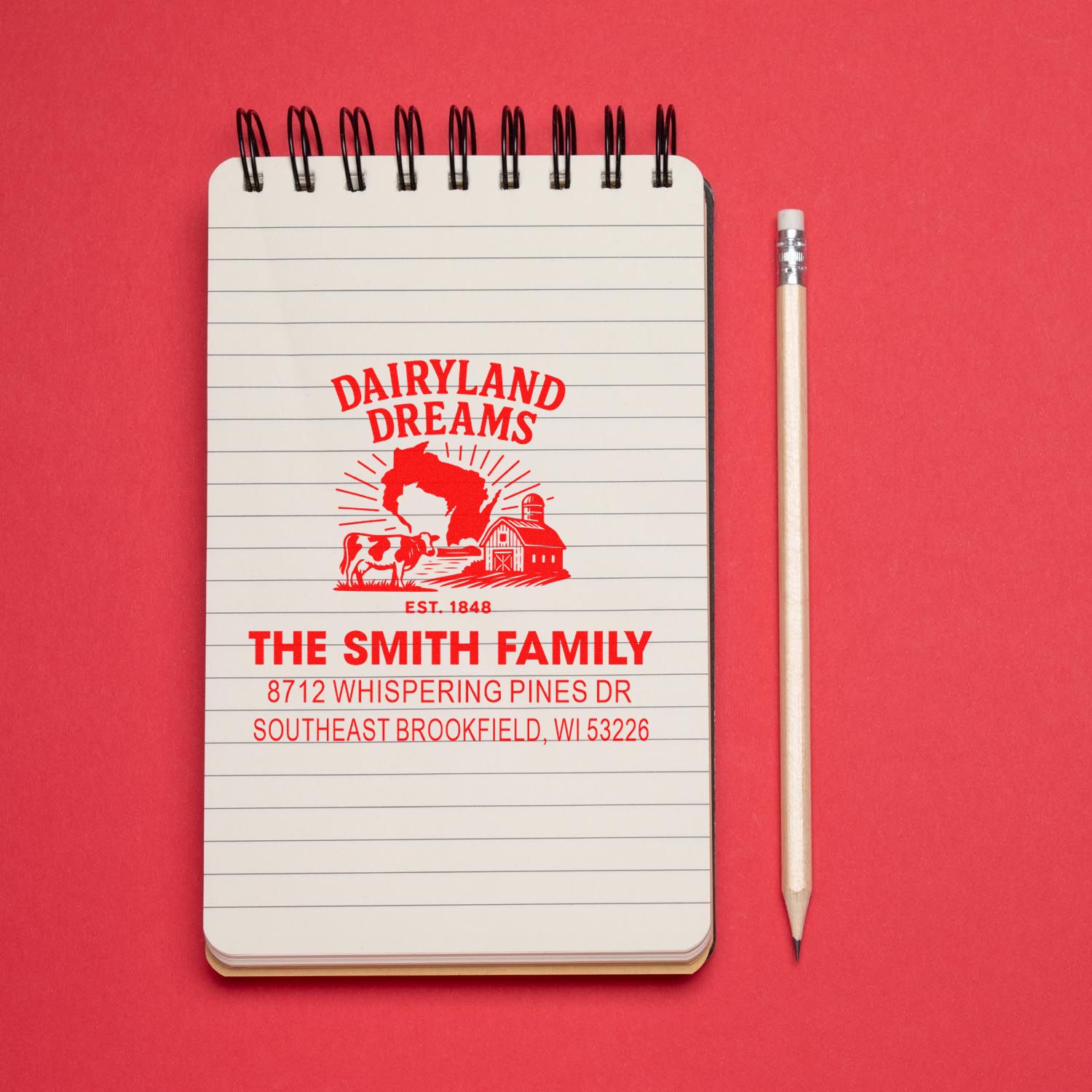 Custom dairy farm address stamp for The Smith Family on lined notepad beside pencil against a red background.