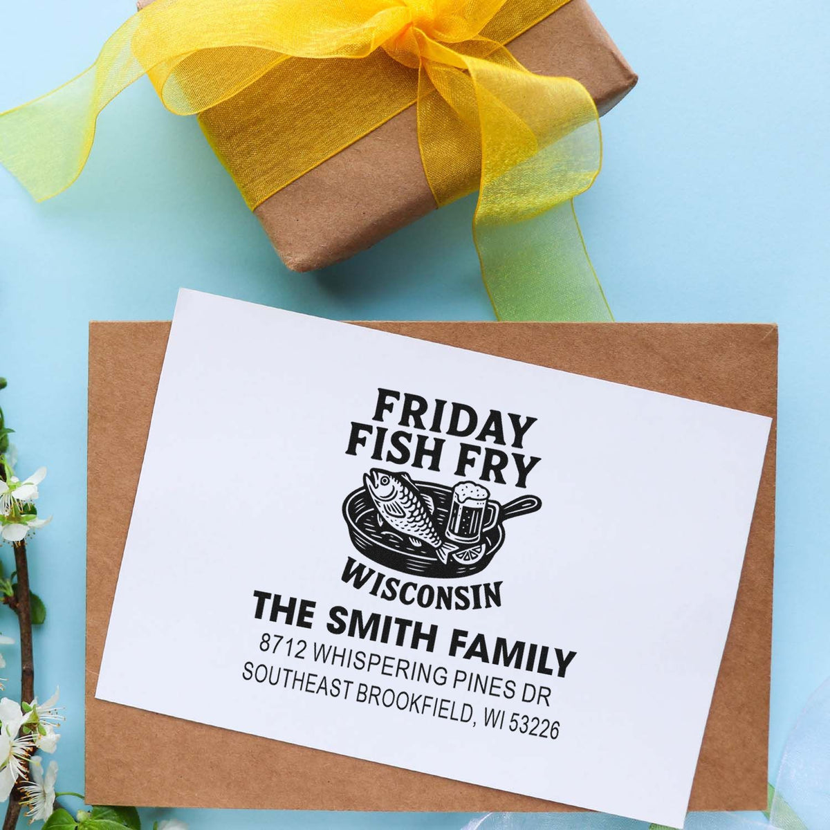 Custom Friday Fish Fry Wisconsin address stamp on kraft envelope beside a yellow-ribbon gift box on a blue background.