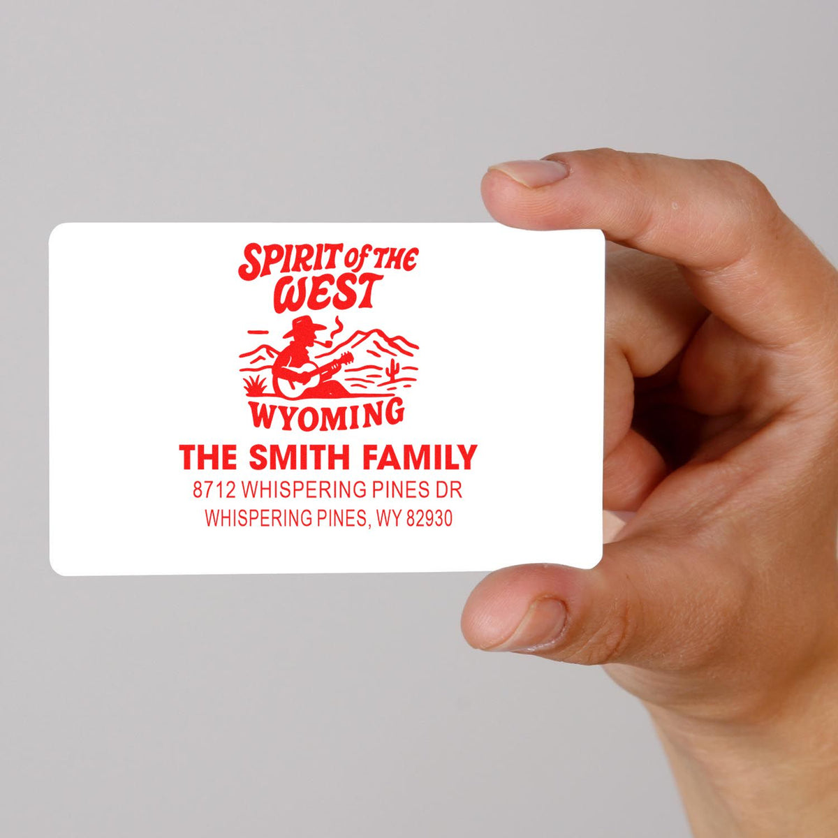 Hand holding custom red return address stamp with Spirit of the West Wyoming cowboy design, Smith Family address on white background.