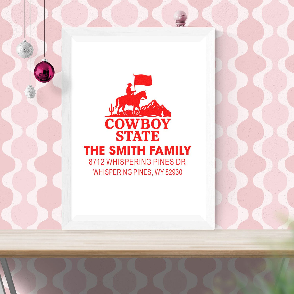 Custom cowboy state family address stamp design in a white frame on pink patterned wall, featuring rider, flag, and red text for The Smith Family.
