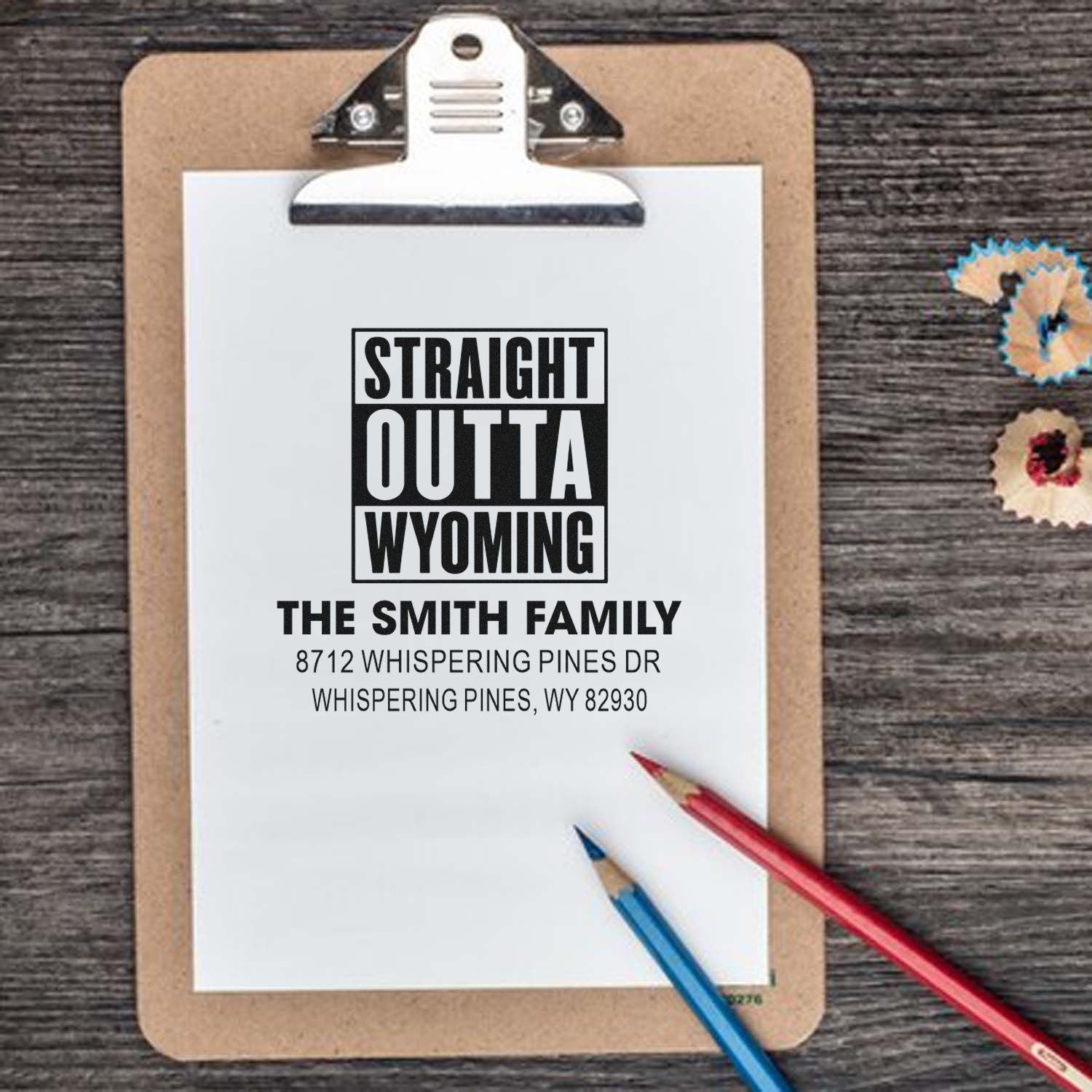 Custom self-inking address stamp on clipboard with Straight Outta Wyoming and Smith family address, on rustic wood table with pencils.