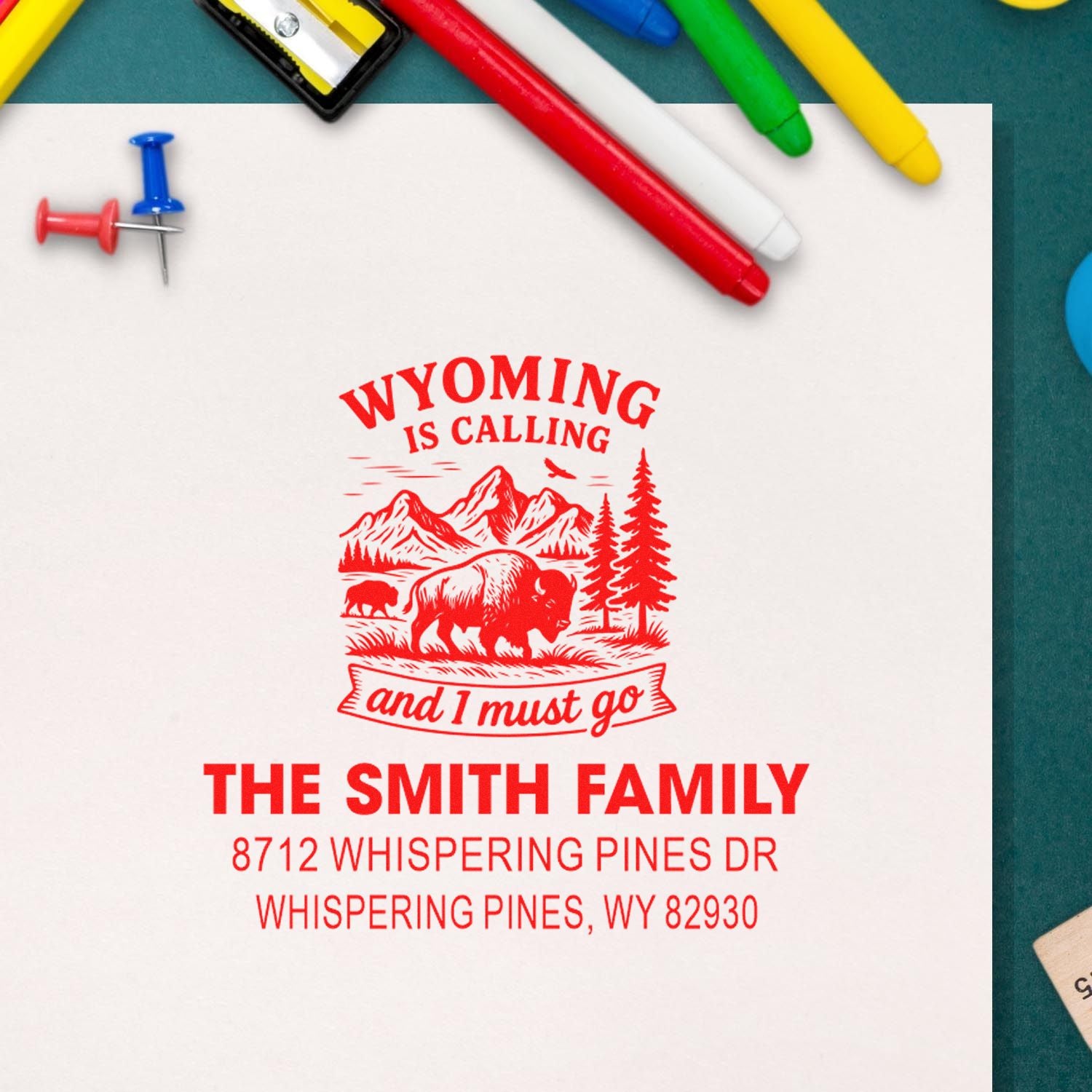 Personalized Wyoming Calling address stamp on white paper, surrounded by colorful pens and pushpins, with bison, mountains and The Smith Family address.