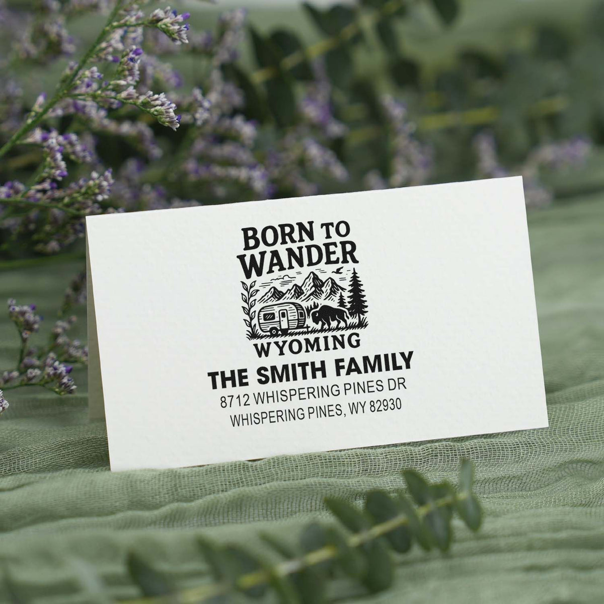Personalized Wyoming return address stamp with Born to Wander mountain, camper, and bison design on a soft green floral background.