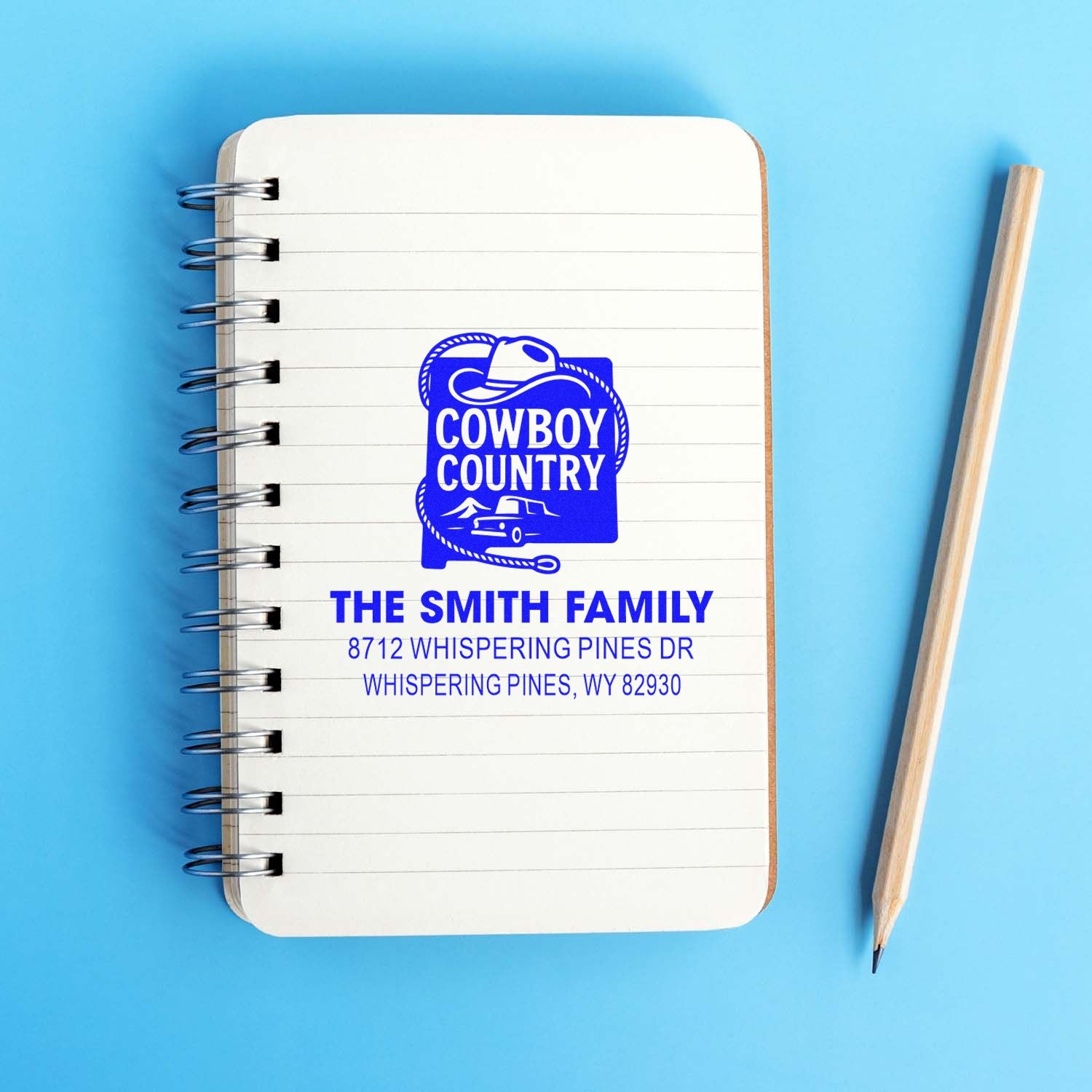Custom cowboy country return address stamp on a spiral notebook with pencil, featuring The Smith Family and a Wyoming address on a blue background.