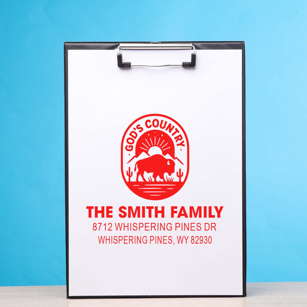 Custom red family address stamp on clipboard with Gods Country bison design, Smith family name and address on white paper against blue background.