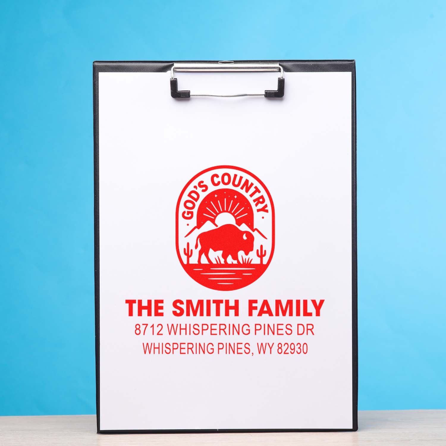 Custom red address stamp on clipboard with bison Gods Country logo and The Smith Family mailing details on a blue background.