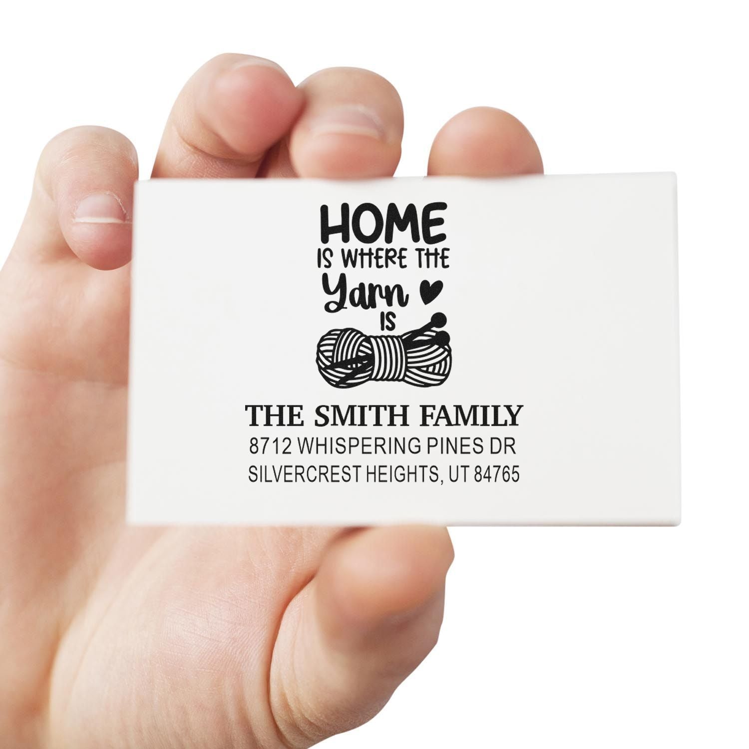 Hand holding personalized return address stamp reading Home is where the yarn is, with yarn graphic and The Smith Family address.