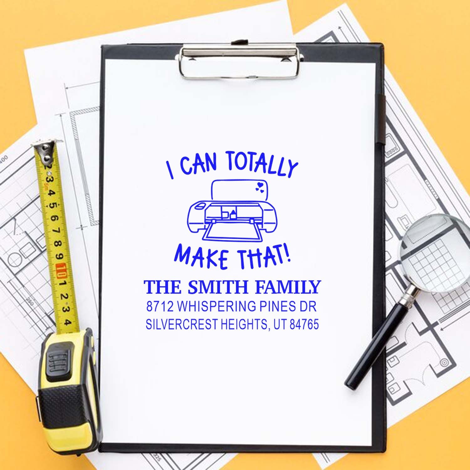 Custom self-inking address stamp on clipboard with I Can Totally Make That! for The Smith Family, beside house plans, tape measure, and pencil.
