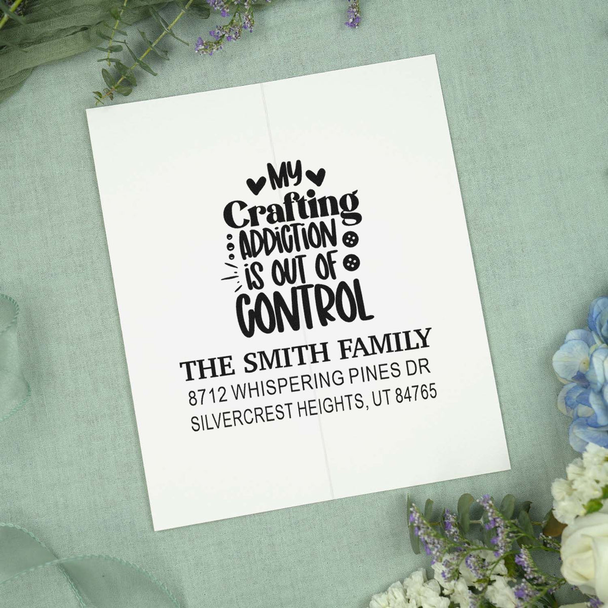 Personalized crafting address stamp on an open card, reading My crafting addiction is out of control, on pastel fabric with flowers.