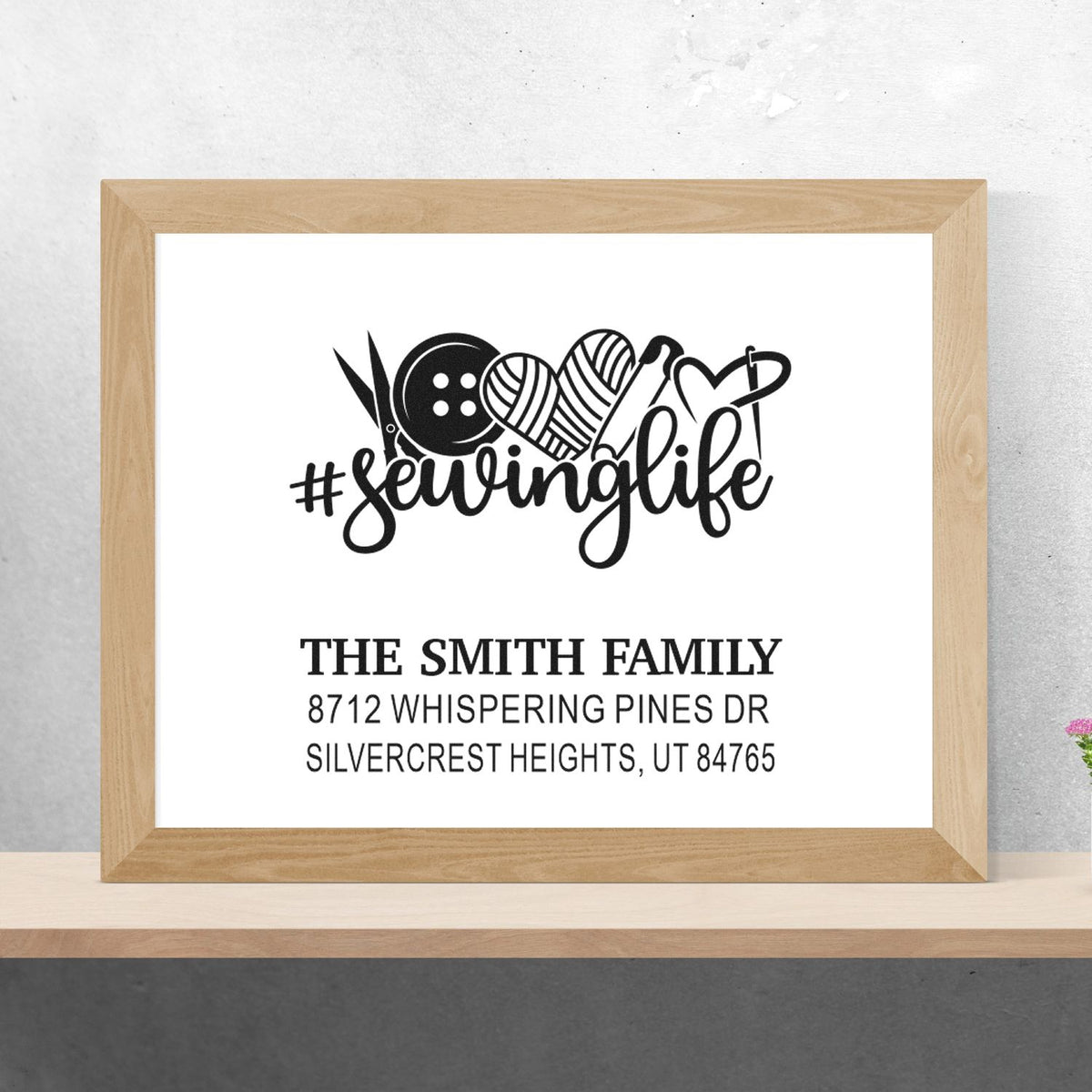 Custom sewing life return address stamp with scissors, button, yarn and heart icons for The Smith Family in a framed mockup.