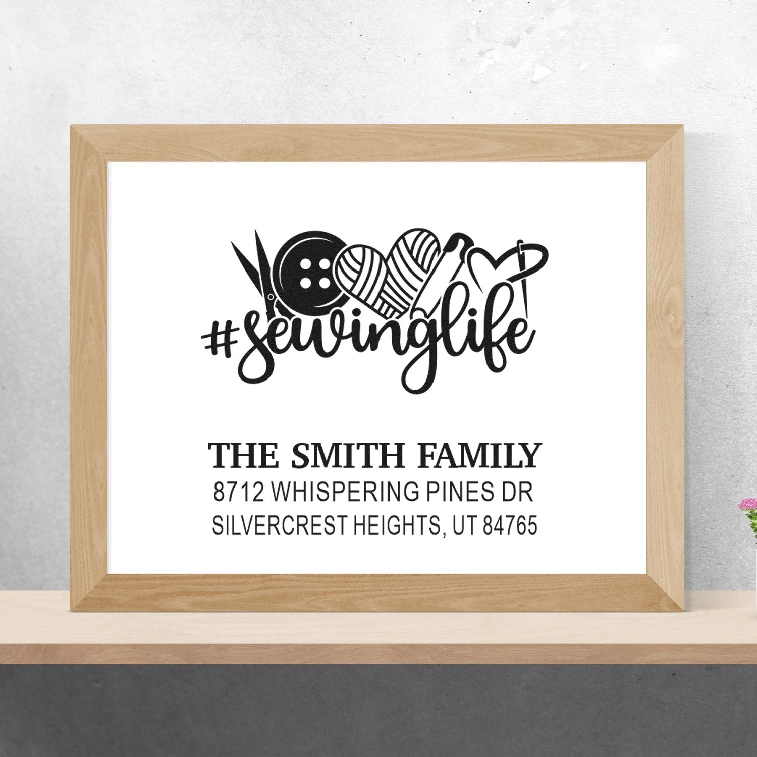 Custom sewing-themed address stamp design with #sewinglife, scissors, button, yarn hearts, and The Smith Family address on a wooden frame display.