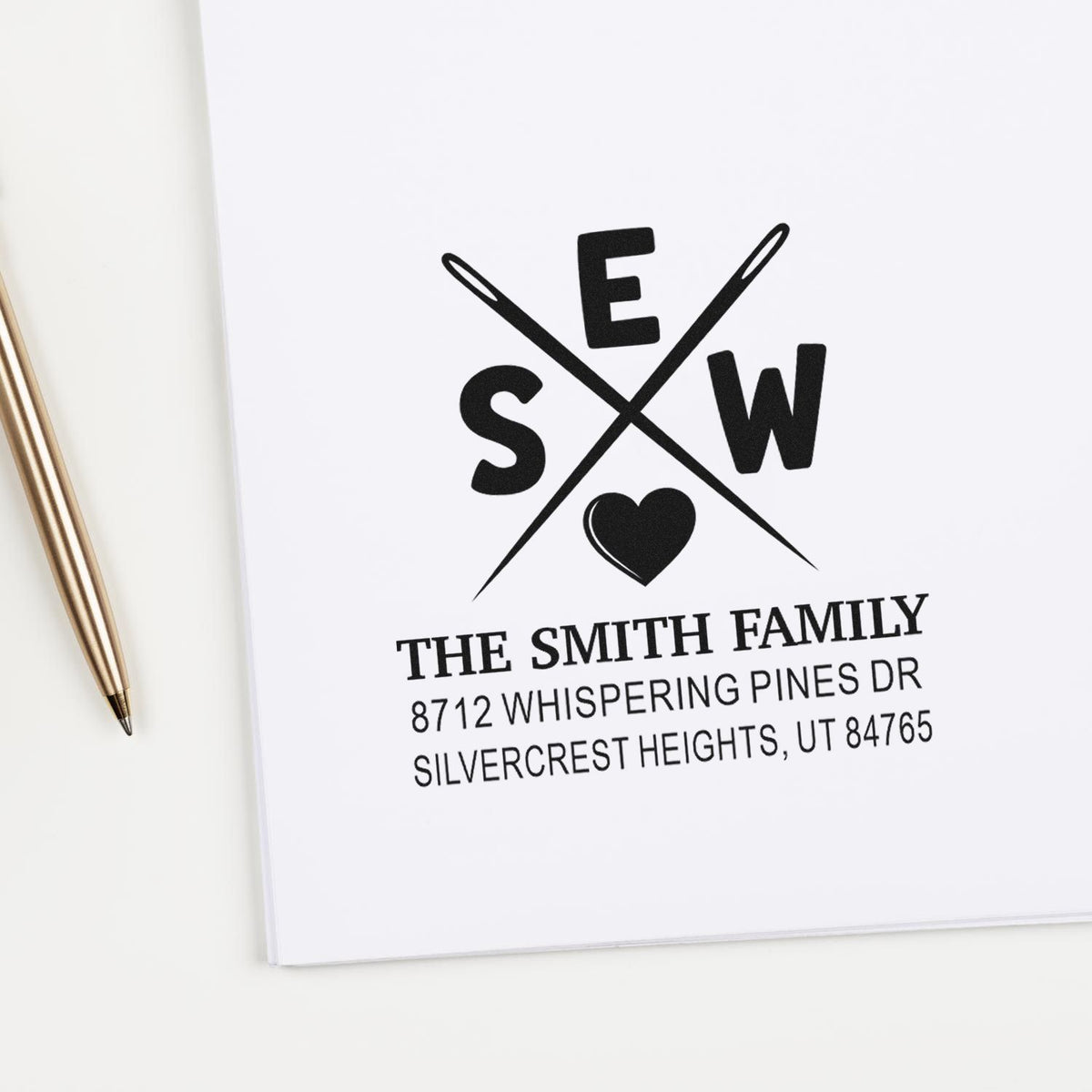 Custom return address stamp with crossed sewing needles, heart, and Smith family name on white stationery beside a gold pen.