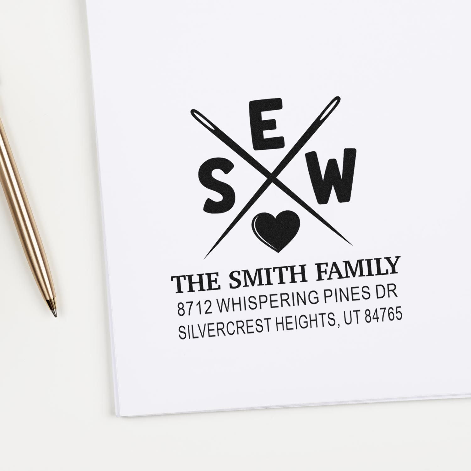 Custom family address stamp with crossed pens and heart logo on white stationery beside a gold pen, featuring The Smith Family address.