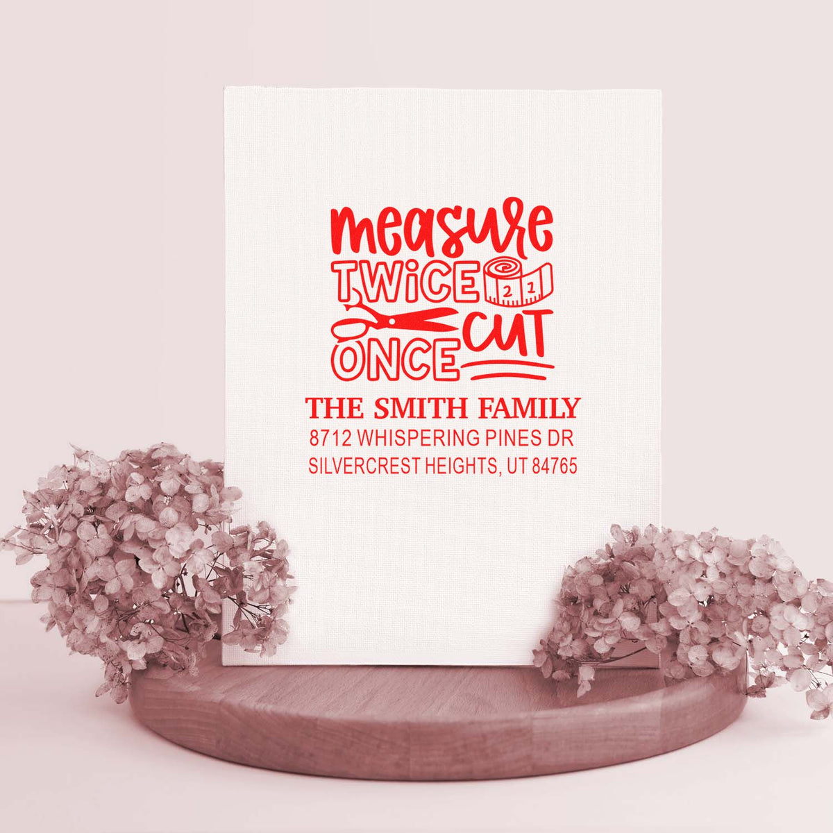 Personalized family address stamp with measure twice cut once scissors and tape measure design, shown on a white display card with pink flowers and wood base.