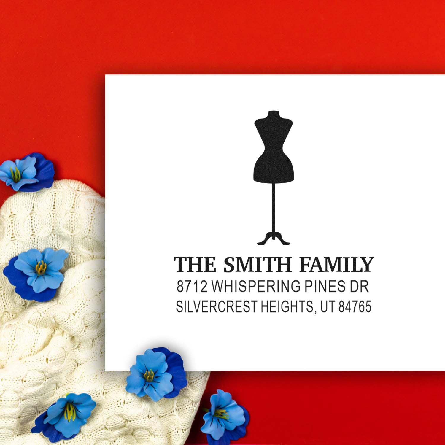 Personalized address stamp for The Smith Family with dress silhouette, shown on a white card against a red background with blue flowers and knit fabric.