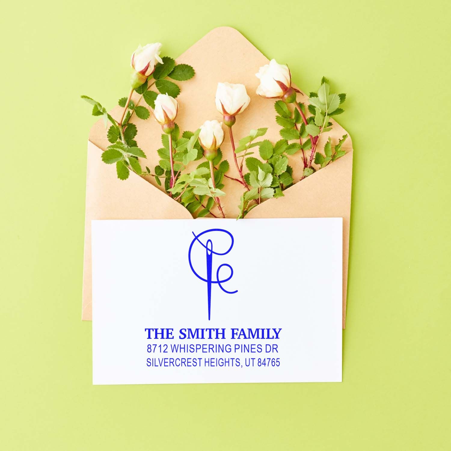 Personalized blue return address stamp on a white card, displayed in a tan envelope with white rose stems on a green background.