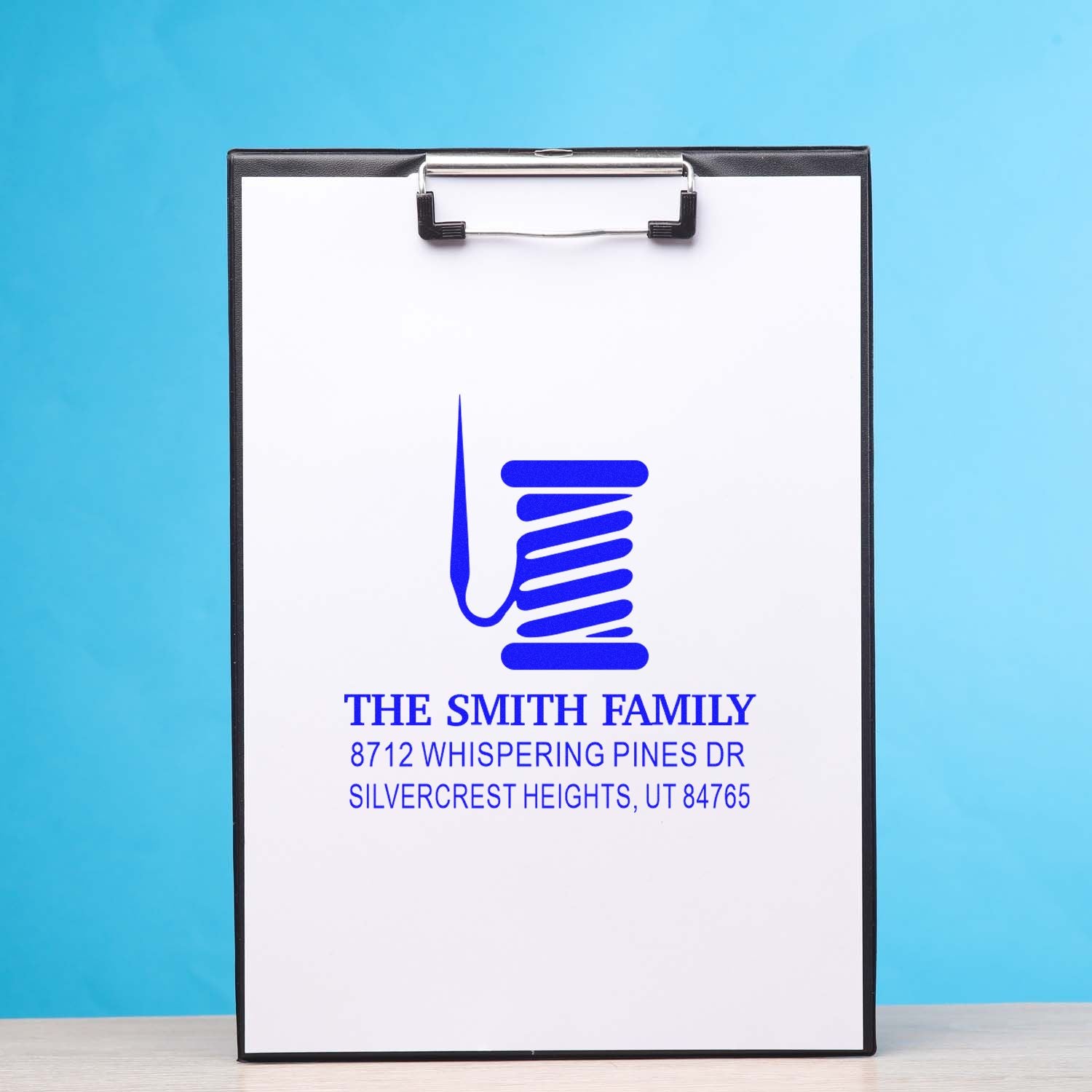 Custom return address stamp on clipboard with blue family name and address, displayed on white paper against a blue background.