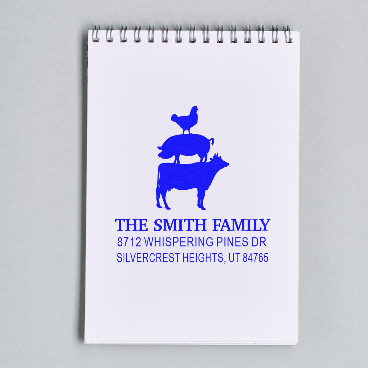 Custom blue family return address stamp with chicken, pig and cow silhouette on a spiral notepad, featuring The Smith Family and Utah address.