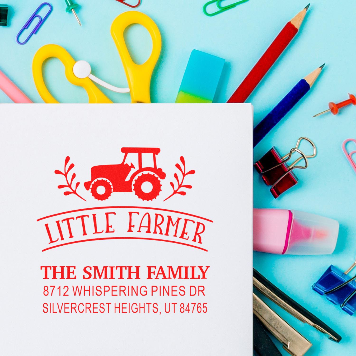 Custom Little Farmer family address stamp on a desk with colorful school supplies, pencils, clips, and stationery.