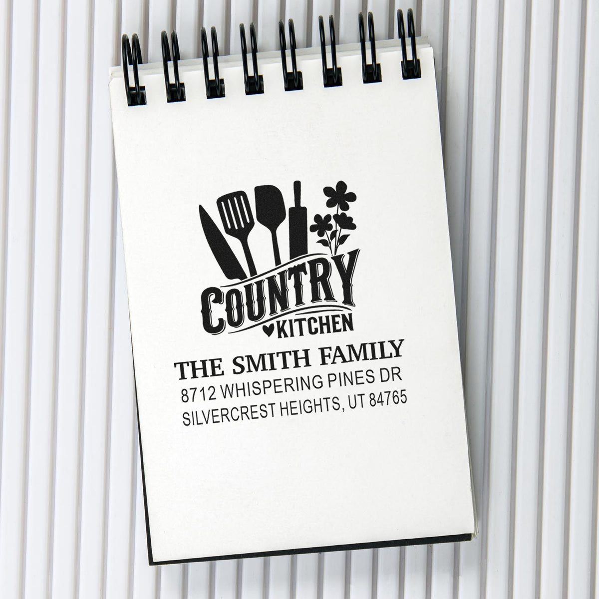 Custom country kitchen address stamp on a spiral notepad, featuring utensils, flowers, and The Smith Family address.