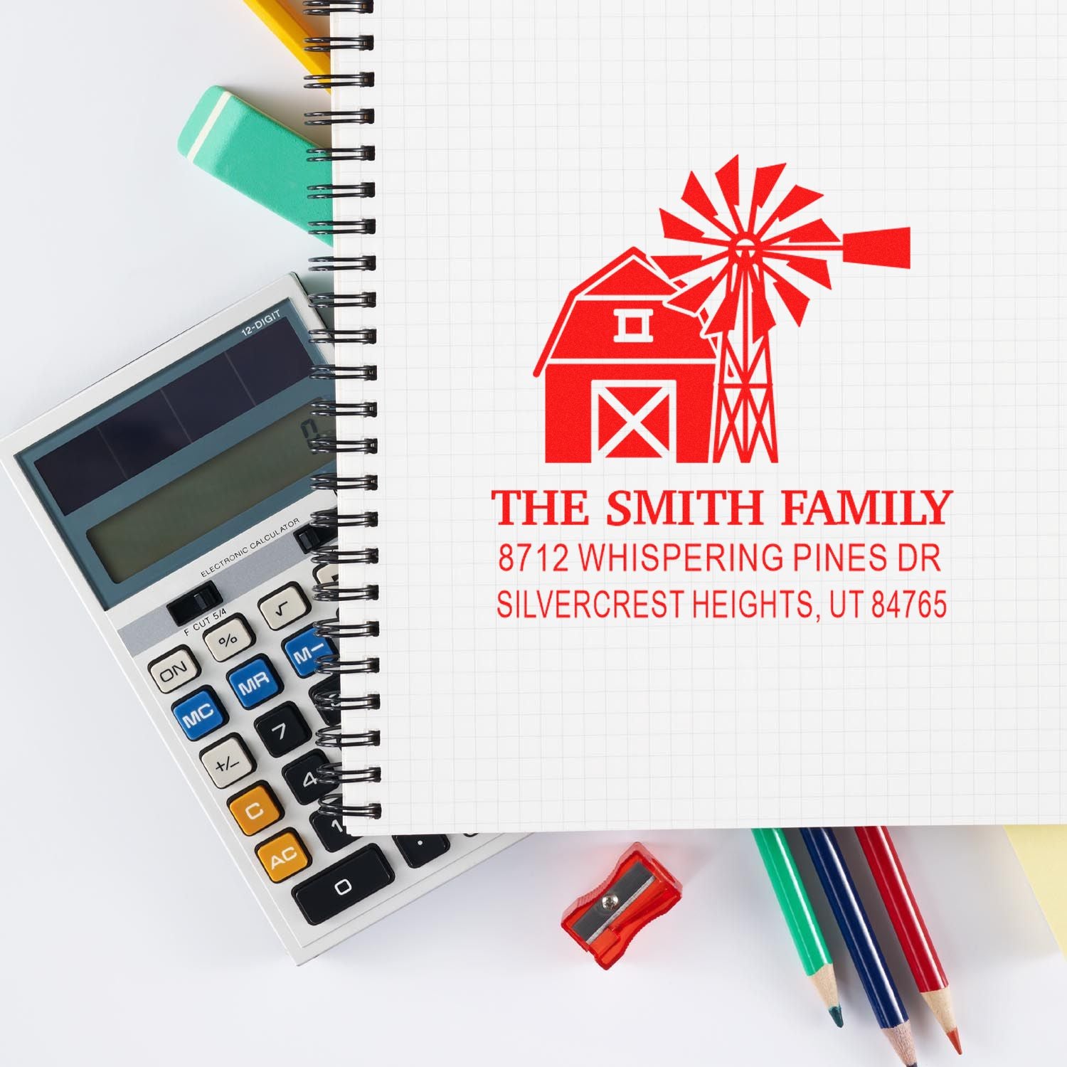Personalized address stamp with barn and windmill design on graph notebook, beside calculator, pencils, and sharpener.