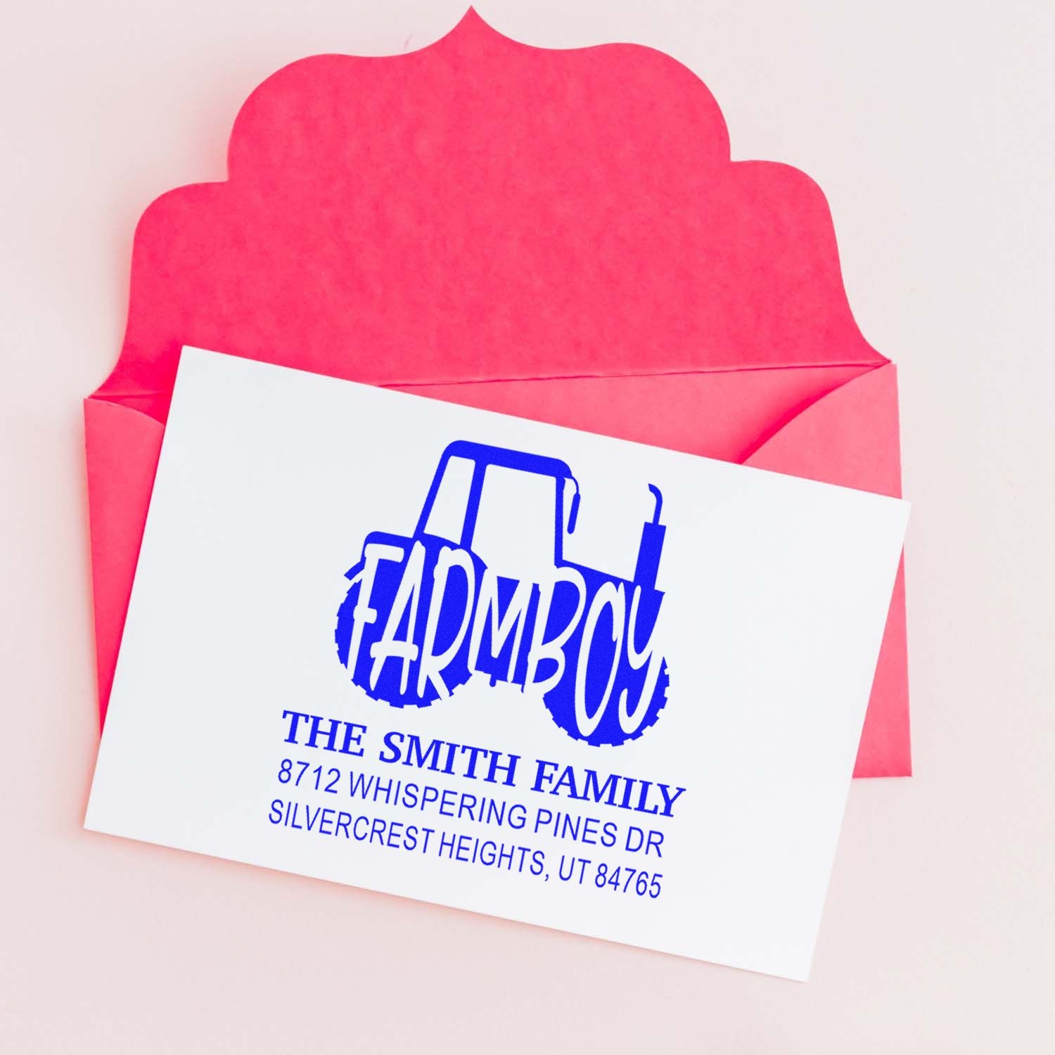 Custom blue farmhouse return address stamp on white card, displayed over a bright pink envelope for mailing and stationery personalization.