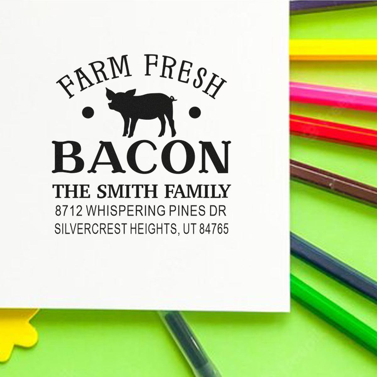 Custom Farm Fresh Bacon return address stamp with pig silhouette, Smith family name, and Utah address on white paper, surrounded by colorful pens.