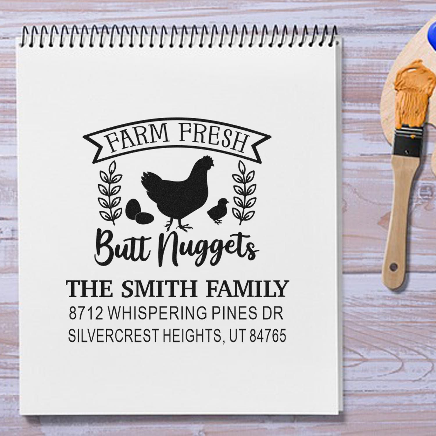 Custom farm fresh chicken return address stamp on notebook, featuring hen, chicks, eggs, family name and address on a wood tabletop with stamp brush.