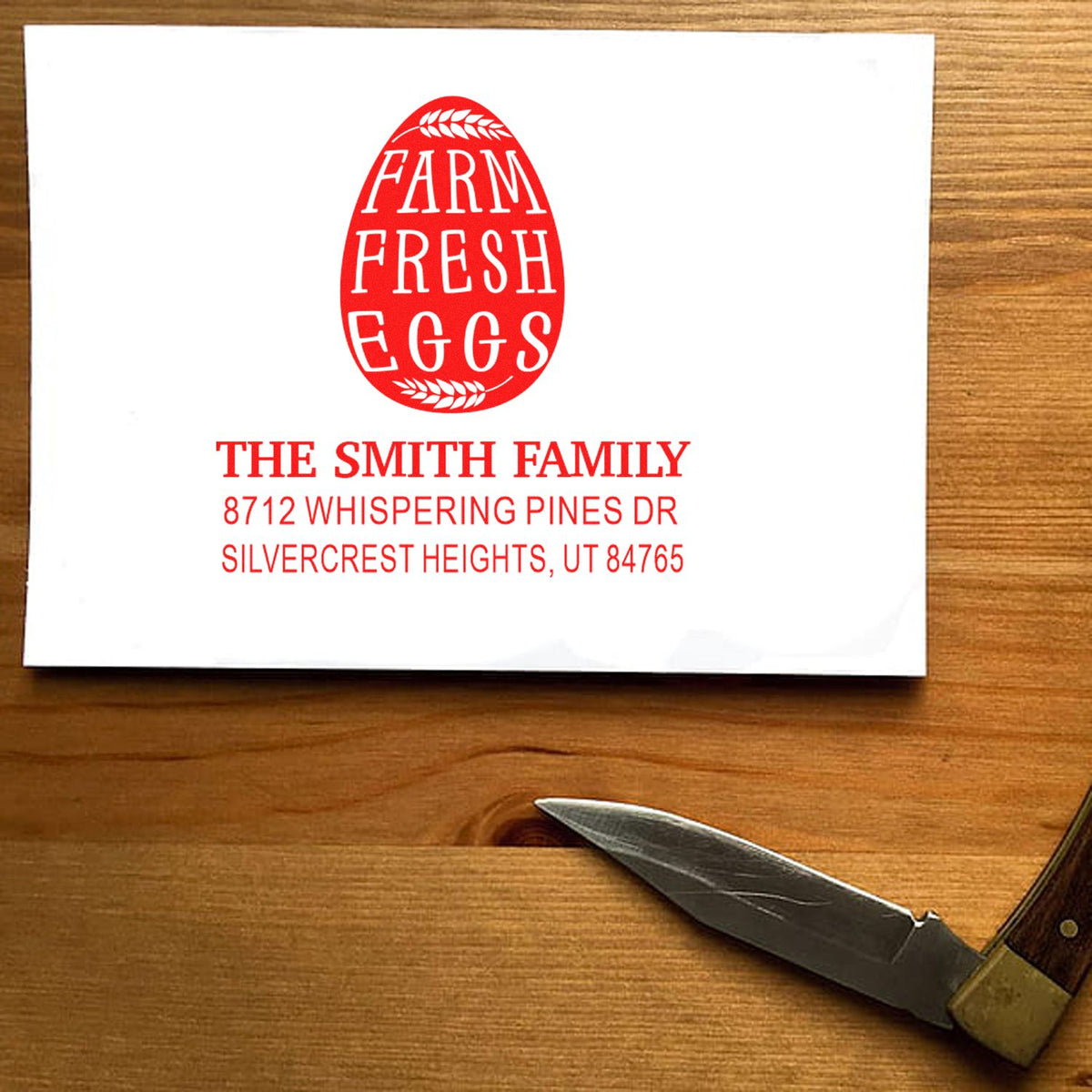Custom farm fresh eggs stamp with The Smith Family name and address, displayed on white paper over a wooden table with a pocket knife nearby.